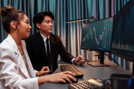 Smiling Asian business traders pointing to dynamic stock exchange data screen profit value online...