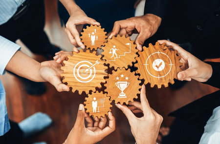 A diverse group of hands coming together to hold wooden gears, symbolizing collaboration and teamwork in business, highlighting goal achievement and strategic planning. Amityの写真素材