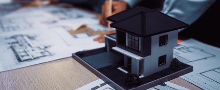 An architectural model sits on a table amid blueprints as designers engage in collaboration. The...