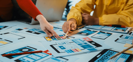 Close-up of a collaborative workspace featuring hands selecting user interface mockups from a table....