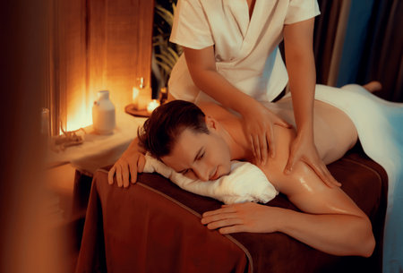 Caucasian man customer enjoying relaxing anti-stress spa massage and pampering with beauty skin recreation leisure in warm candle lighting ambient salon spa at luxury resort or hotel. Quiescentの写真素材