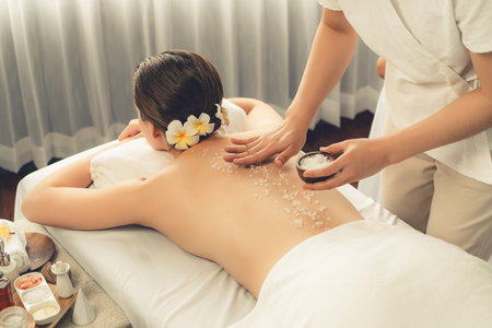 Woman customer having exfoliation treatment in luxury spa salon with warmth candle light ambient. Salt scrub beauty treatment in health spa body scrub. Quiescentの写真素材