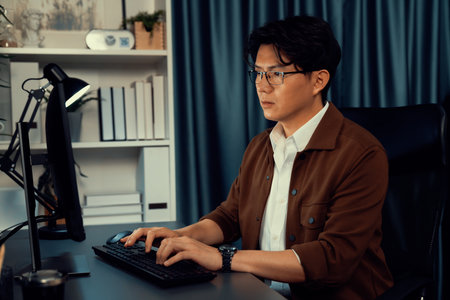 Businessman in casual attire focusing on computer to create business plan report late at night in office, working on market planning with new company project.の写真素材