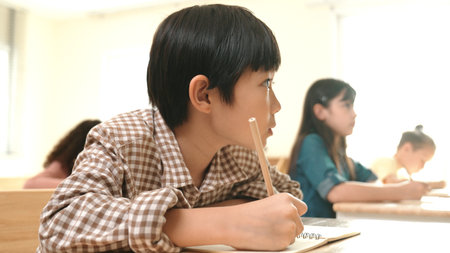 Close up of skilled asian student writing or taking a note during test. Elementary student working on paper while multicultural doing classwork or homework at classroom. Education concept. Pedagogy.の写真素材
