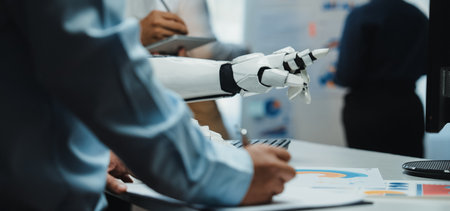 A human hand writing notes while a robotic hand gestures, showcasing collaboration in a modern office while working on technology and data analysis projects.の写真素材