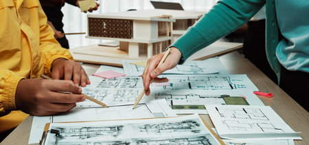 A vibrant architectural design meeting showcases hands actively sketching blueprints and analyzing models, reflecting teamwork and creativity in a dynamic workspace environment.の写真素材