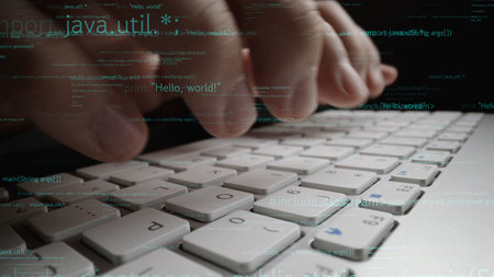 Close-up view of hands typing on a laptop keyboard, featuring programming code overlay. Ideal for...