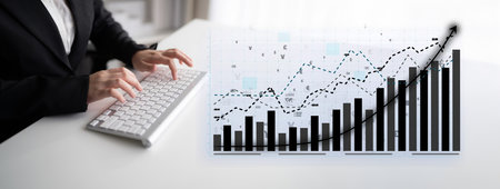 A businessperson engages with financial data on a computer while analyzing graphs that depict...
