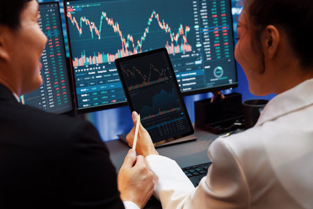 Businesswoman holding tablet on dynamic stock exchange statistic online showing to partners to share, comparing with high or low on computer screen at night neon modern office at back side.の写真素材