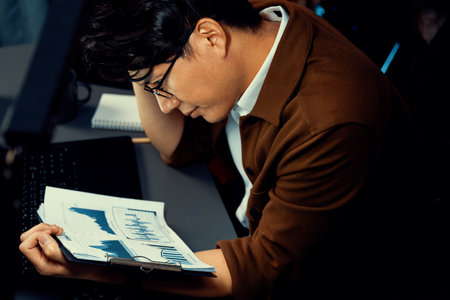 Serious face managers looking on paperwork marketing plan graph to make promotion analysis with social media online at late night at home office.の写真素材