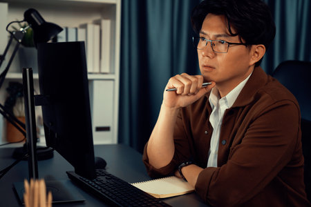 Businessman in casual day focusing computer to create business plan report over late night time at office, working on searching tools market planning with new startup company project.の写真素材