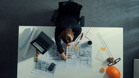 Top view of civil engineer using ruler and equipment to measure blueprint. Architect working while working on laptop with sticky notes and calculator to design building construction.の写真素材