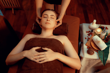 Caucasian woman enjoying relaxing anti-stress head massage and pampering facial beauty skin recreation leisure in warm candle lighting ambient salon spa in luxury resort or hotel. Quiescentの写真素材