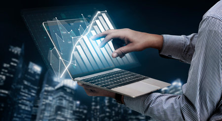 A person hand interacts with a touchscreen laptop displaying a virtual financial graph, symbolizing...