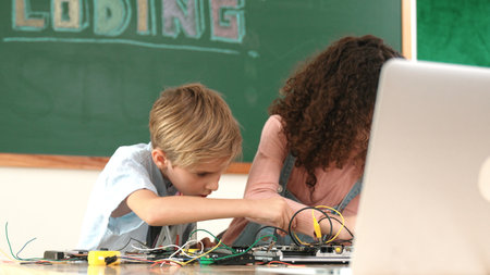 Diverse smart student working together to fix main board at stem class while looking at laptop...