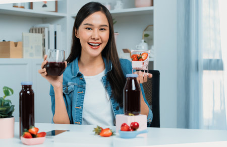 Smiling young beautiful Asian reviewing tasty mixed strawberry and cherry juice detox drinks, showing healthy product to promote for special promotion selling on social media online record.の写真素材