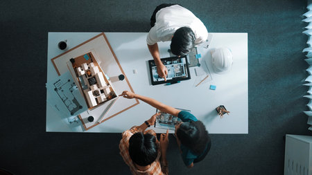 Top down view of civil architect looking at project plan while present to investor at meeting table. Aerial view of skilled designer explain about construction to business people listen.の写真素材