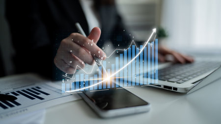A business professional conducts data analysis in a modern workspace, utilizing a laptop and smartphone while focusing on digital graphs and trends for strategic insights. Imputeの写真素材