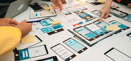 A team of designers collaborates on user interface designs using smartphones and tablets in a...