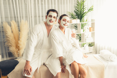 Blissful couple in bathrobe with facial cream mask enjoying serene ambiance of spa salon resort or hotel during holiday. Pampering face spa and skincare treatment with essence relaxation. Quiescentの写真素材