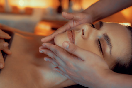 Closeup caucasian woman enjoying relaxing anti-stress head massage and pampering facial beauty skin recreation leisure in warm candle lighting ambient salon spa in luxury resort or hotel. Quiescentの写真素材