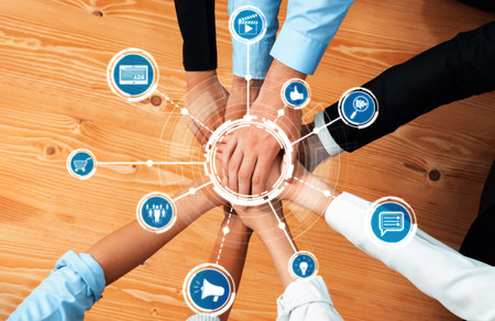 Hands of diverse professionals come together in a modern workspace, symbolizing teamwork,...