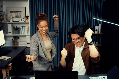 Successful smiling business trader with partner in casual suit earning high profit raising fist up in exchange stock market investment in technology at modern office at night.の写真素材