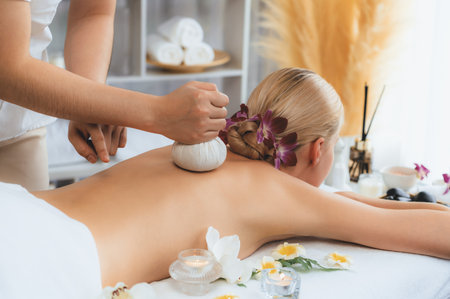 Hot herbal ball spa massage body treatment, masseur gently compresses herb bag on woman body. Tranquil and serenity of aromatherapy recreation in day lighting ambient at spa salon. Quiescentの写真素材