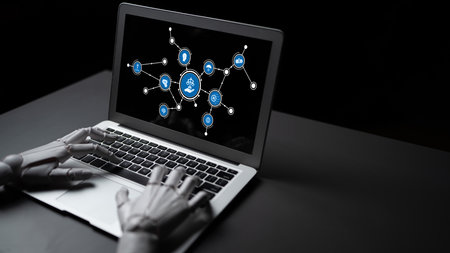 A robotic hand interacts with a laptop displaying icons of technology and innovation on a dark background, symbolizing the future of automation and digital connectivity. Tesselの写真素材