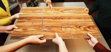 A group of diverse hands collaboratively holds a wooden puzzle on a table, symbolizing teamwork and strategic planning during a dynamic problem-solving session.の写真素材