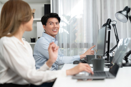 Smiling Asian man talking with woman colleague in planning marketing report project on laptop casual day while searching database on working desk at modern home office at side view image. Infobahn.の写真素材