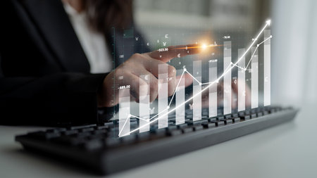 A business professional engages with digital financial graphs while analyzing data on a keyboard, representing modern technology role in data-driven decision-making. Imputeの写真素材
