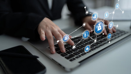 A focused businessman interacts with a modern laptop, showcasing digital icons that represent various online services and technology in a contemporary office setting. Tesselの写真素材