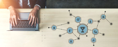 A modern workspace featuring hands typing on a laptop with a visual diagram of success and achievement icons, representing business goals and strategic planning. Tesselの写真素材