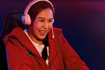Portrait of a beautiful Asian girl streamer playing an online game wearing headphones in a pastel color, talking with viewers online. Esports skilled team players in a neon blue room.の写真素材