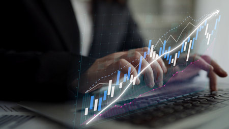 A business professional uses a laptop to analyze financial data, with a digital graph overlay...