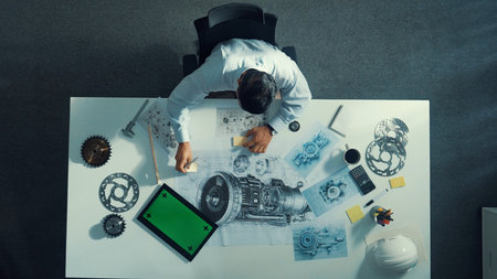 Top down view of skilled engineer writing and planning turbine engine design while sitting at meeting table with gear and electronic generator scatter around. Technician taking a note.の写真素材