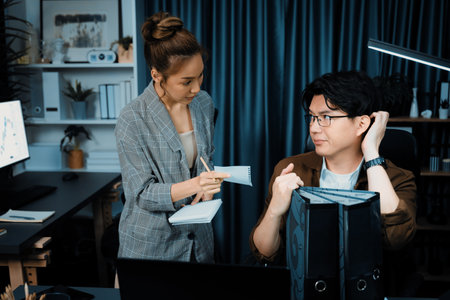 Serious face of manager with coworker discussing overworked folder paper at over late night, writing check list memo of collected signing document for board company keeping database file. Infobahn.の写真素材