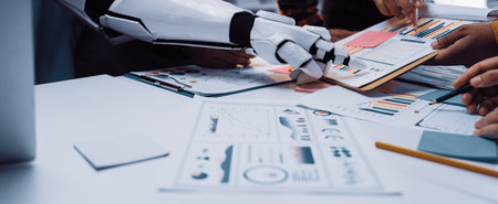 A robot arm assists a human team during a collaborative meeting, analyzing data reports and charts on the office table, highlighting the future of teamwork in business.Noogenesisの写真素材