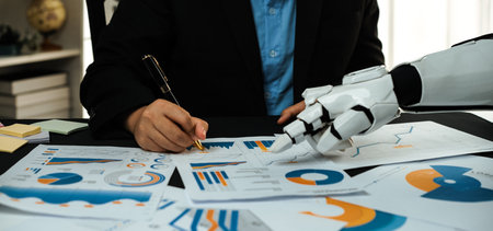 A business professional collaborates with a robot assistant while analyzing detailed charts and graphs, showcasing the blend of technology and innovation in a modern workspace.の写真素材