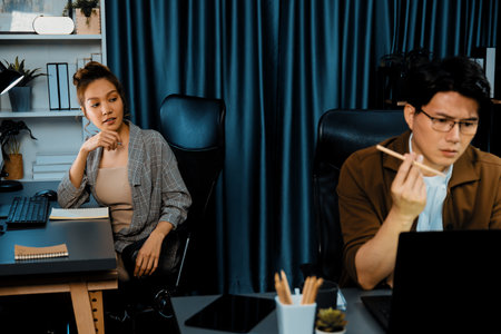 Businessman with stressful face working on laptop waiting email while coworker discussing together for consult at late night time at modern office, working on startup company project job. Infobahn.の写真素材