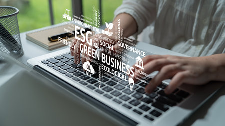 A focused business professional works on a laptop while surrounded by words related to ESG practices, emphasizing the importance of sustainability and governance in modern business. Tesselの写真素材