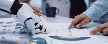 A robot hand collaborates with a human hand over charts and documents in a modern office, showcasing...