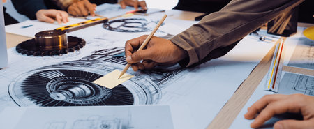 A group of engineers engaged in a collaborative session focusing on technical drawings of mechanical components, showcasing hands-on work with precision tools and detailed planning.の写真素材