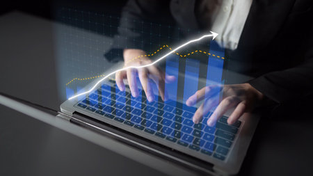 A professional individual types on a laptop while analyzing financial data and growth trends,...