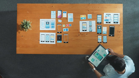 Top down view of software developer holding tablet while choosing icon for mobile phone interface or...