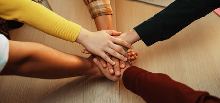 A group of diverse individuals joins hands in a unified gesture, symbolizing teamwork and support in...
