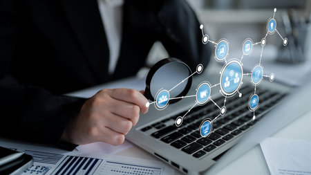 A business professional uses a magnifying glass to analyze data displayed on a laptop in a modern...