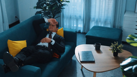 Stressful boss look at decrease sales from laptop and lies on sofa. Professional tired project...