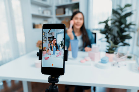 Selective focus smartphone with young beautiful Asian reviewing cosmetic makeup brush cheek test...